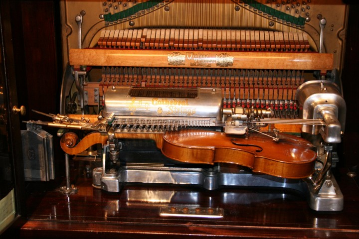 Picture showing a small string instrument clamped inside a mechanism reminiscent of the inside of a piano.