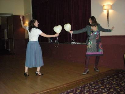 Two members take fencing positions opposite each other, armed with heart shaped balloons.