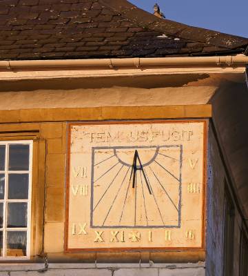 Photo of a sundial clock built-in to the face of a building with the words 'Tempus Fugit' above it.