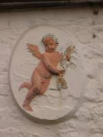 A white plaque of a young male child with angel wings in pink.
