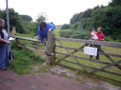 Jo is clambering over a fence next to a gate. The gate has a sign on it saying 'Private Property - No public access'