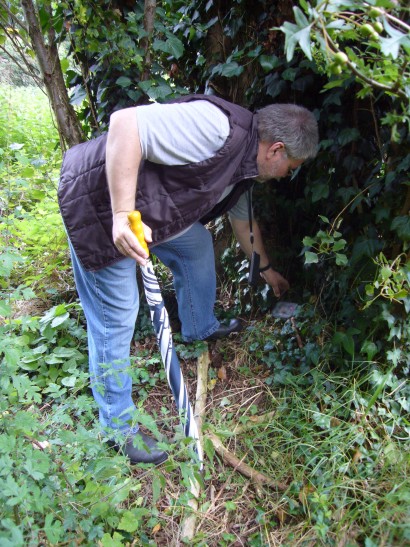 Having found the cache under a large tree, Chris stoops topick it up.