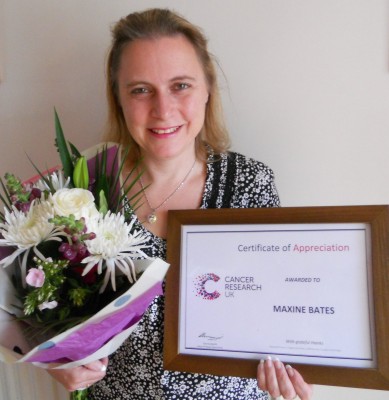Maxine poses smiling, holding her certificate of appreciation in her left hand, and a bouquet of flowers in her right,