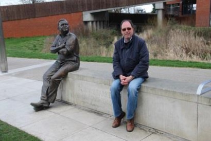 Richard Allen sits on a concrete bench, alongside a bronze statue of Ronnie Barker