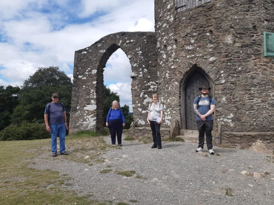 Four members stand, socially distanced, in front of a fortified building