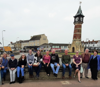 Eleven mensans sit on a wall in front of tower in Skegness