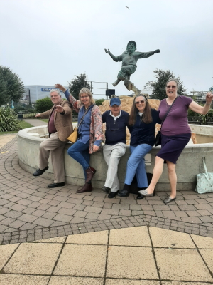 Five members stand in front of a statue in Skegness, emulating the kicking pose of the statue.
