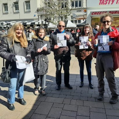 The group stand in the center of Loughborough holding their guide booklets on a bright, sunny day