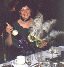 Picture of Clare Price hold her prize bottle of wine and the winning mask with 3 huge white feathers coming from the top of it.