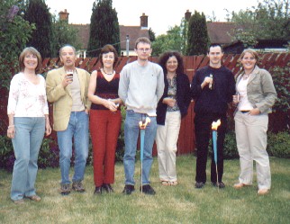Picture of a group of 7 East-Mids mensans at the garden party in Letchworth. Two of the men are standing directly behind the garden flares which are just less than waist high giving an interesting line of site effect. 